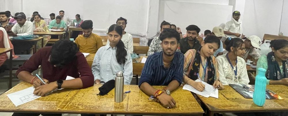 Students attending a classroom session, actively writing notes at their desks.